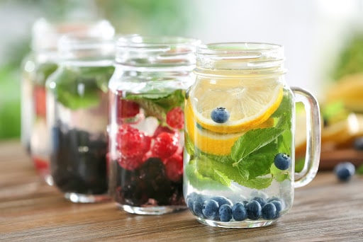 Mason jars of infused water with fruits and berries on wooden table