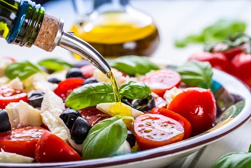 Caprese Italian or Mediterranean salad. Tomato mozzarella basil leaves black olives and olive oil on wooden table.