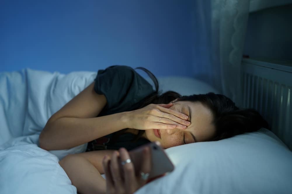 Woman lying In Bed sleepless holding smartphone In hand