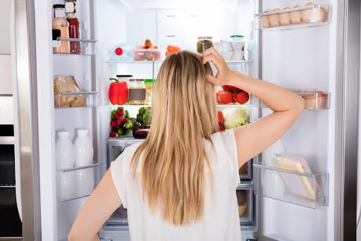 Young lady standing in front of the open fridge, not knowing what to eat.