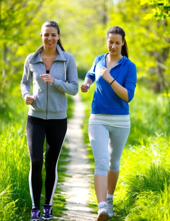 During the evening, two women leisurely stroll along a path nestled between vast grass fields.