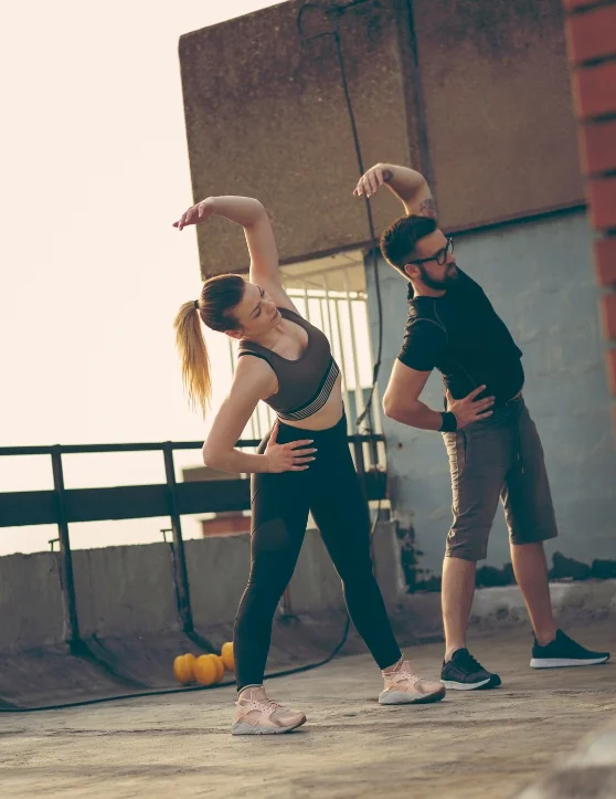 The boy and girl are engaging in warm-up exercises on an open terrace