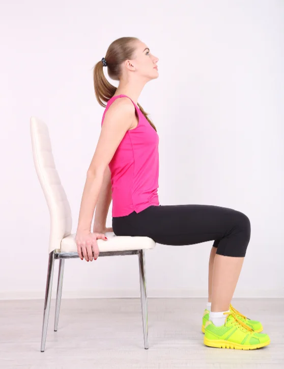 The girl is practicing chair yoga, dressed in a pink top and black pants. With her legs firmly placed on the floor, she holds onto the chair with both hands, finding balance and serenity in the poses.
