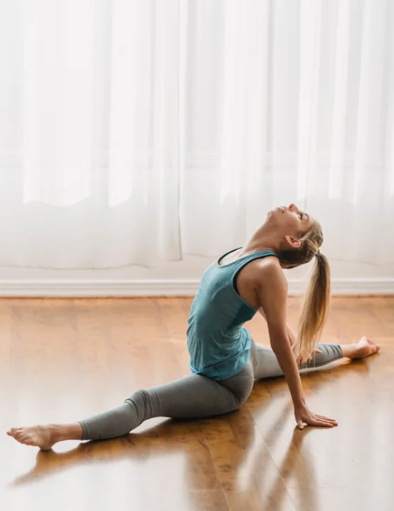 The woman is performing a stretchable yoga exercise on the floor in an indoor setting