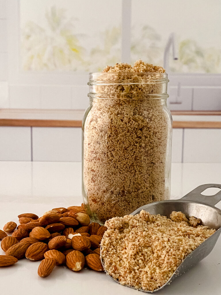 Ground Raw Almonds Filled In A Glass Jar With A Scoop And Raw Almonds Aside