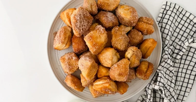 air fryer cinnamon sugar biscuit bites in a white plate beside checked towel