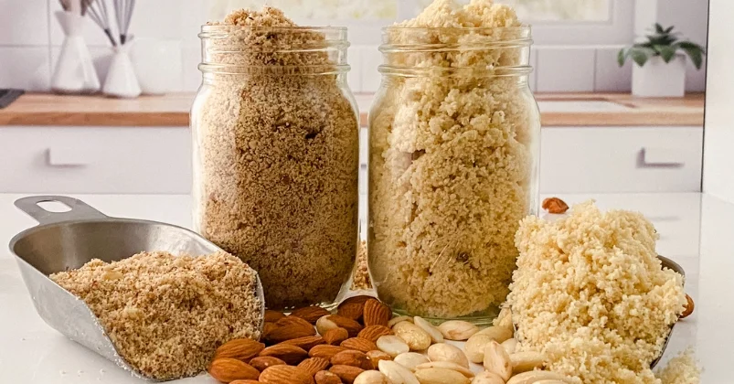 freshly ground raw and blanched almond flour filled in glass jars along side freshly ground almond flour in scoops, raw and blanched almonds