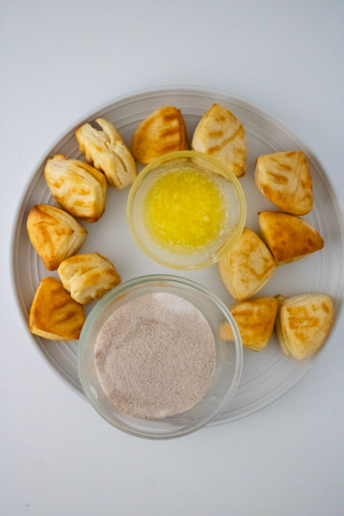fried biscuits placed on the glass plate along with cups of cinnamon sugar and butter