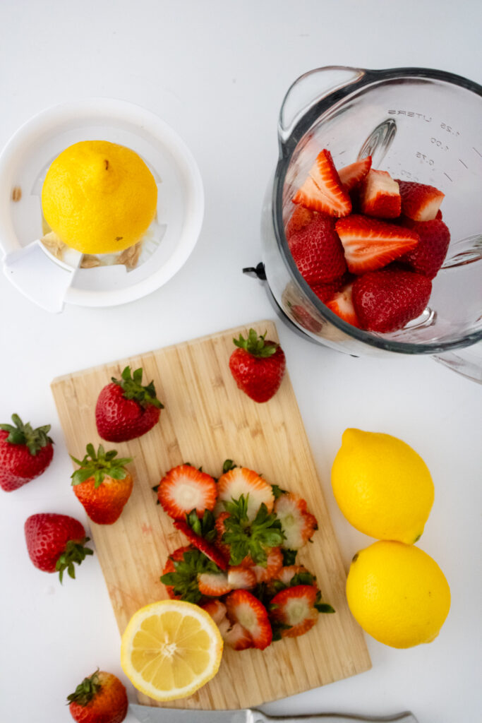 cut strawberries on a wooden cutting board with lemons to the side to make strawberry lemonade