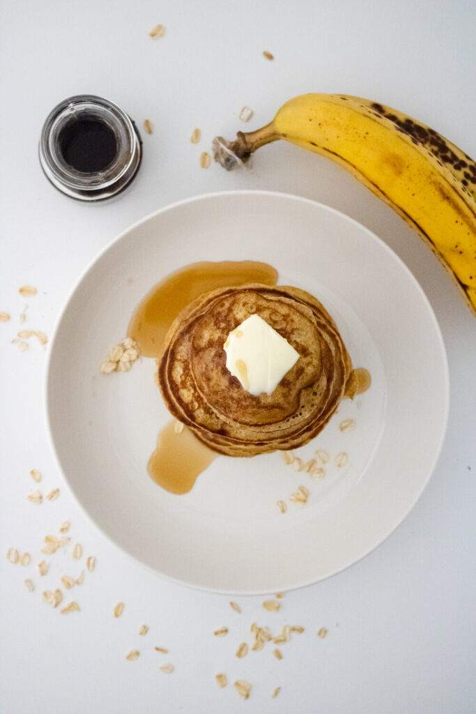 banana oat pancakes with butter topping placed on serving plate alog side banana and honey