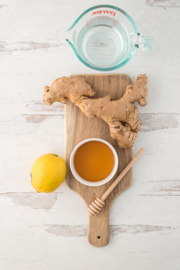 cup of water along with ginger on wooden chopping board and lemon