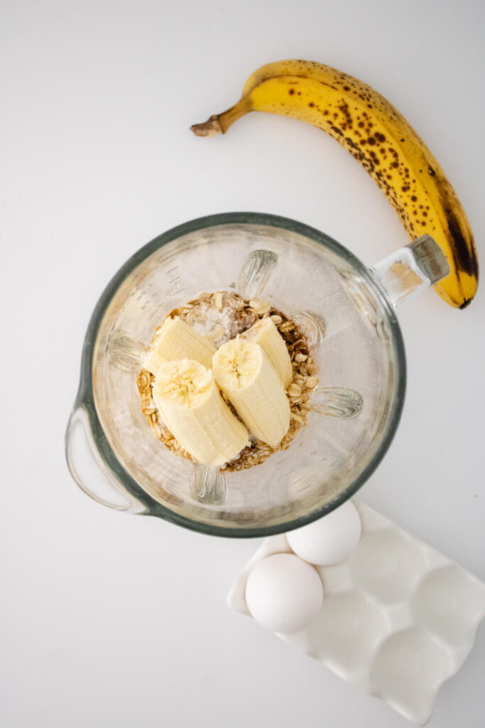 cut pieces of banana, milk, vanilla extract, rolled oats, baking powder, ground cinnamon, salt and olive oil in blender along side two eggs in the holder