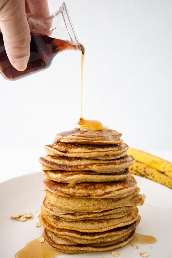 honey poured on stacked banana oat pancakes with butter on top placed on white plate