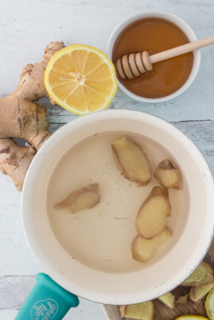 slices of ginger inside boiling water along with lemon and honey in a small cup