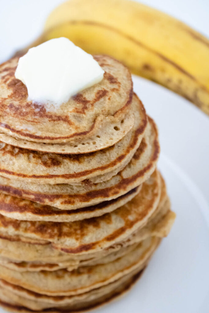 stacked banana oat pancakes with butter on top placed on white plate