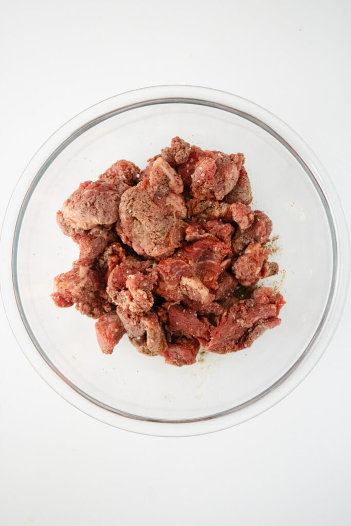stew meat mixed with ingredients in glass bowl