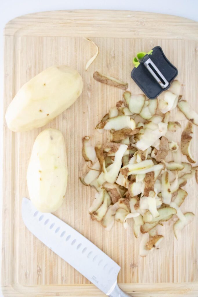 peeled boiled potatoes with knife and peeler on wooden cutting board