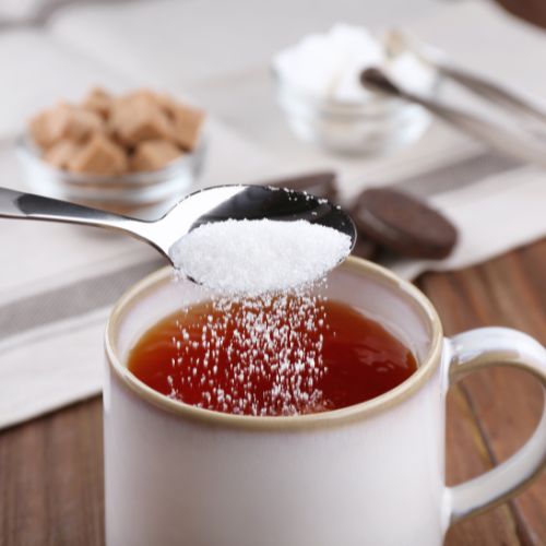 Sugar is being poured onto a black tea in a white glass