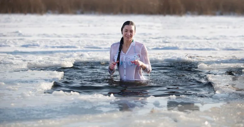 The girl is standing in freezing cold plunge water, wearing a white shirt, while taking a cold bath