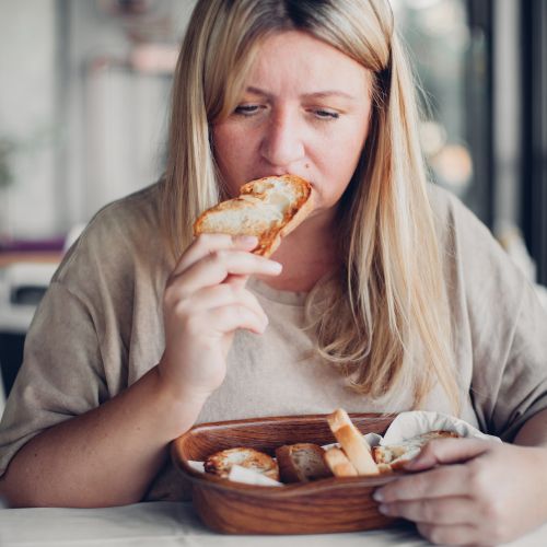 The girl, wearing a t-shirt, has a sad expression while eating bread