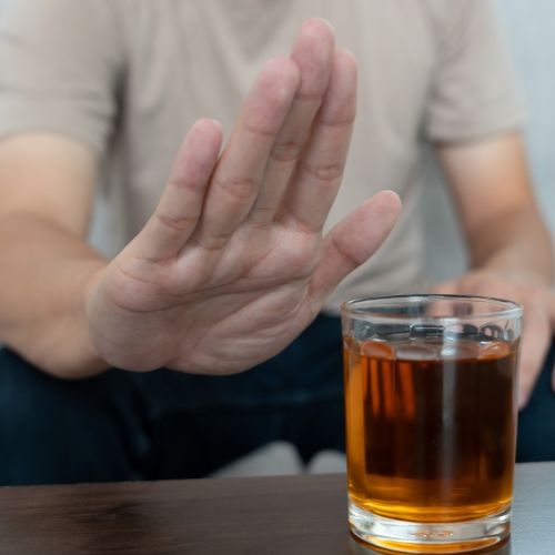The man is gesturing with a stop hand signal towards alcohol