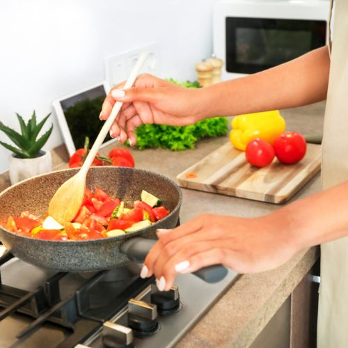 The woman is cooking with a pan filled with vegetables