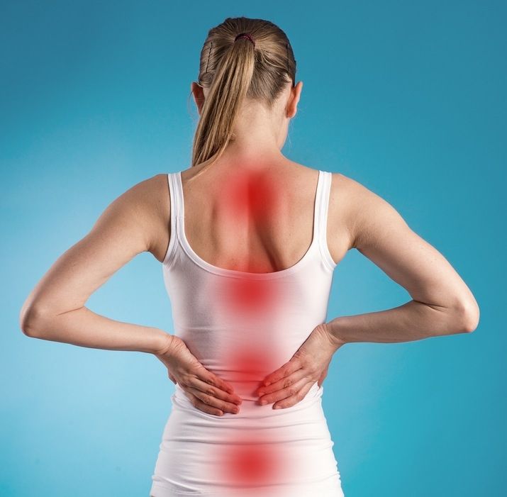 A girl wearing a white dress is holding her back with her hands against a blue background