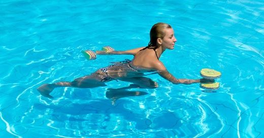 A woman performs water exercise with foam dumbbells in a pool as part of aqua fitness