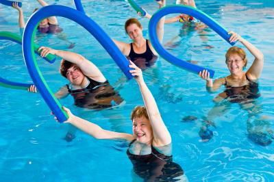 group of older adults participating in a water exercise class using pool noodles as a part of their workout