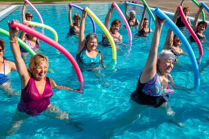 image features a group of elderly women participating in a water aerobics class using pool noodles