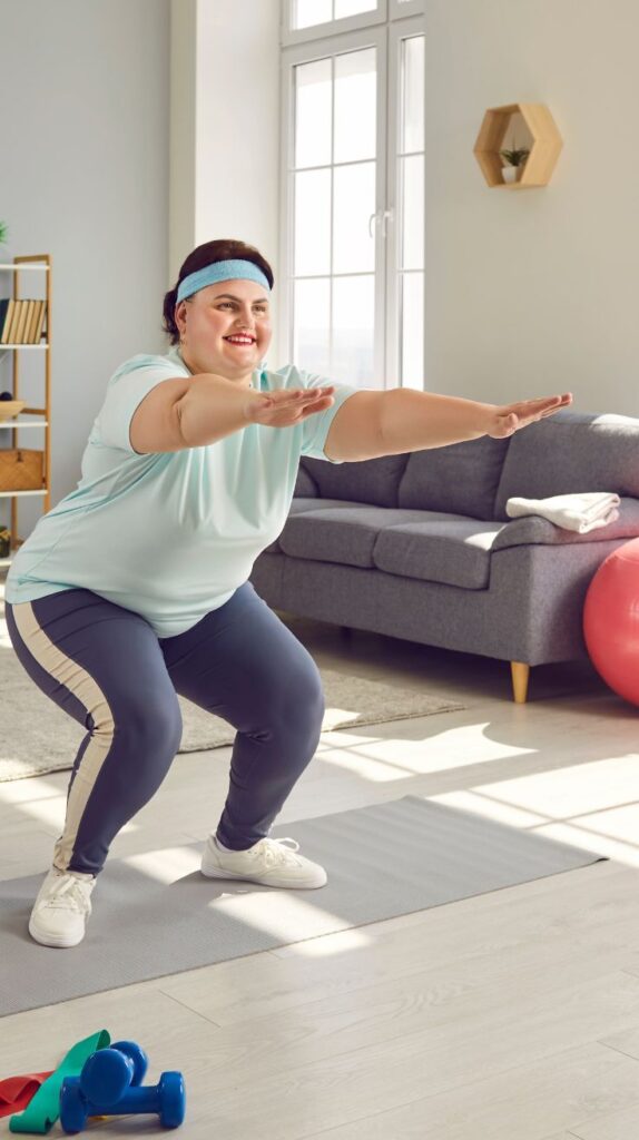 A smiling person in activewear performs a squat exercise at home on a yoga mat, with dumbbells and resistance bands nearby