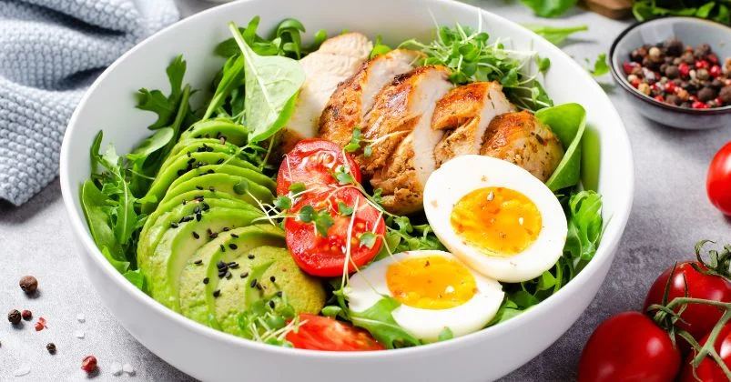 fast on semaglutide, bowl of fresh, colorful salad containing grilled chicken slices, avocado, tomato, leafy greens, and boiled eggs, garnished with black sesame seeds