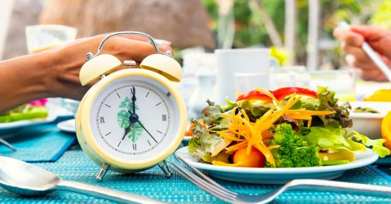 yellow clock next to a plate of fresh salad symbolizing Intermittent fasting